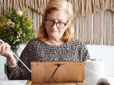 Mujer haciendo tranquiamente nudos con un tapiz de fondo